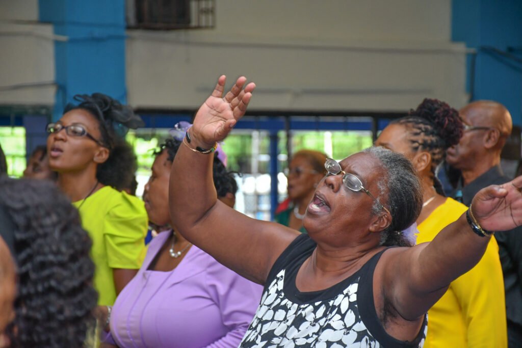 A group of people in a church setting, with one woman enthusiastically raising her hands in worship or praise, showcasing expressions of joy and spirituality.