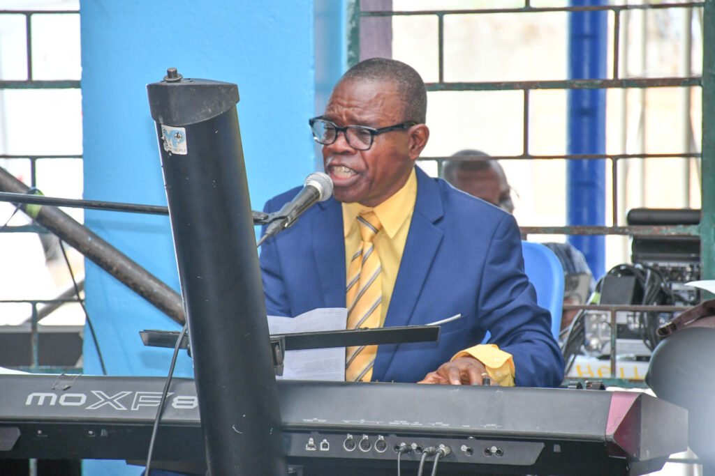Man in a blue suit and yellow shirt playing a keyboard while singing into a microphone.