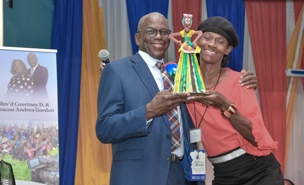 A man and a woman smiling together, holding a colorful trophy, in front of a decorative backdrop with colorful drapes.