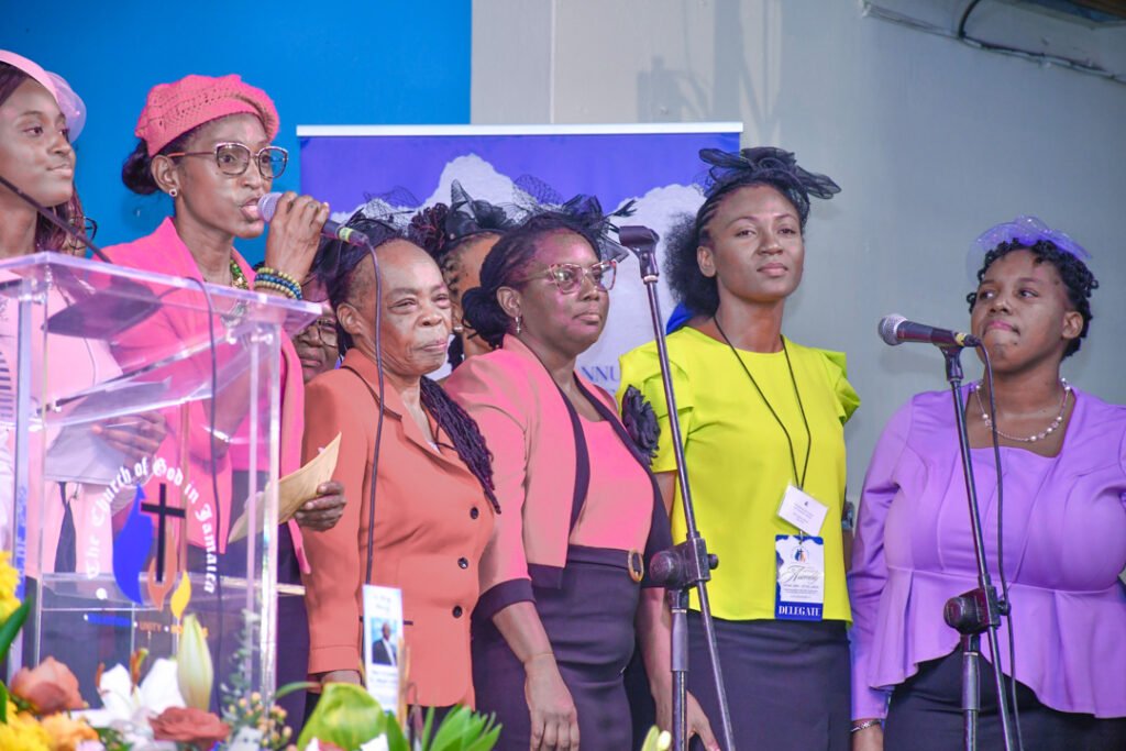 Group of women singing at a church event, with colorful outfits and a podium in the foreground.