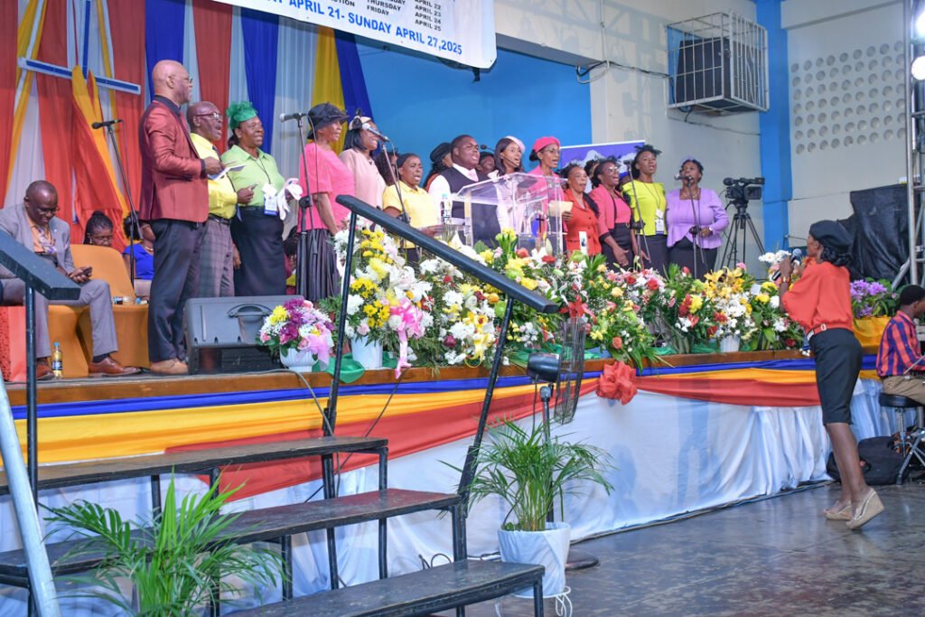 A vibrant choir performing on stage during a church event, surrounded by colorful decorations and floral arrangements.