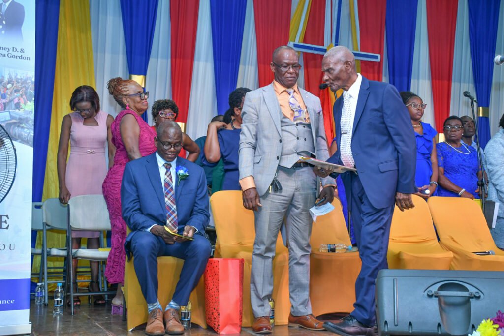 A group of people dressed in formal attire gathered in a colorful decorated venue, engaging in conversation while some individuals sit in the foreground.