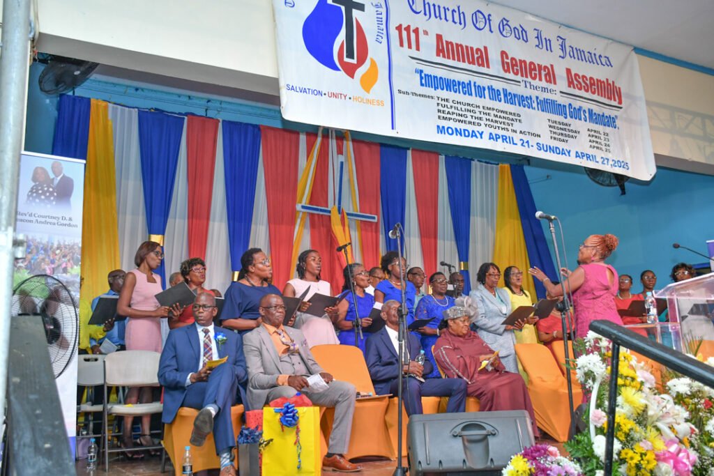A choir performing at the 111th Annual General Assembly of the Church of God in Jamaica, featuring colorful decorations and a banner with the event's theme.