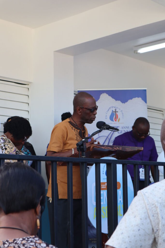 A man speaking at a podium during a formal event, with attendees listening in the background.