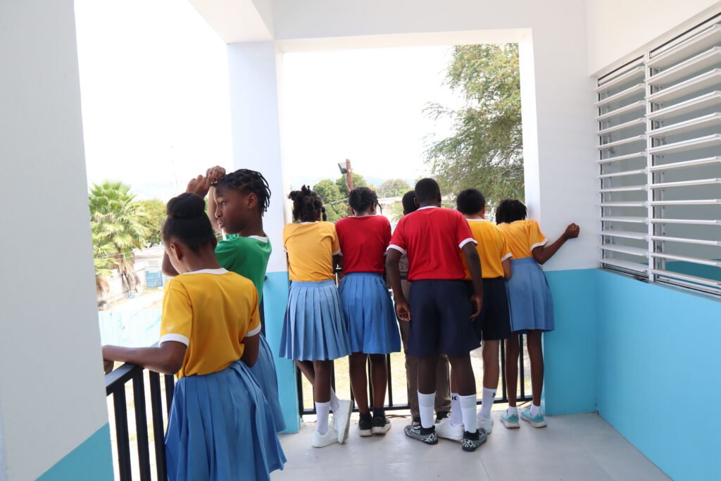 A group of schoolchildren in colorful uniforms leaning over a balcony, looking out at a view.