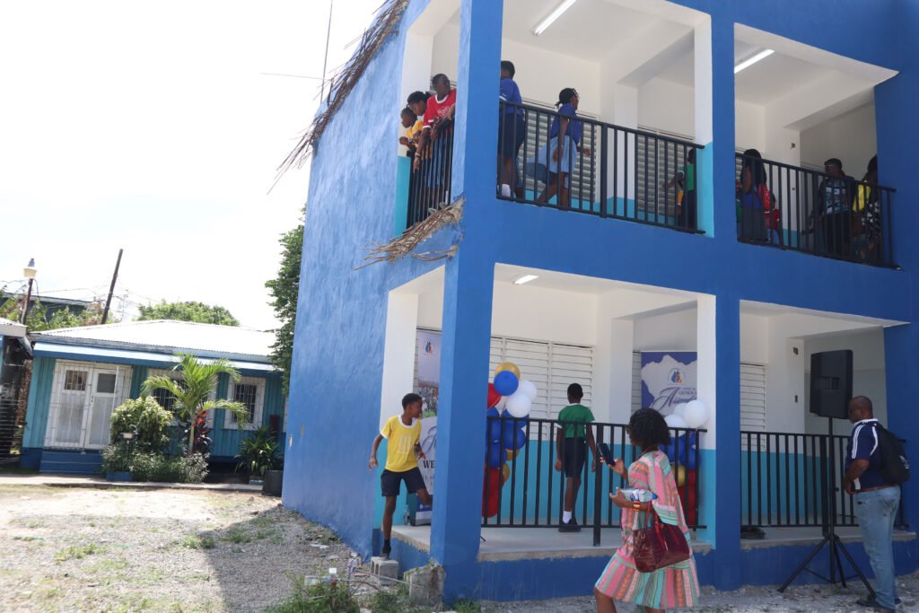 A vibrant blue building with people on balconies and children interacting outside. Some individuals are wearing colorful clothing, and there are decorative balloons in the vicinity.