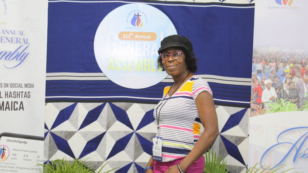 A woman stands smiling at a photo backdrop for the 111th Annual General Assembly, featuring blue and white geometric patterns.