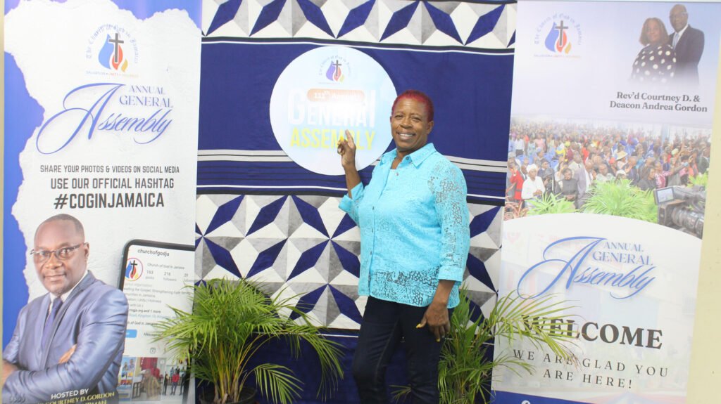 A woman in a blue shirt stands next to banners promoting an annual general assembly event, with images of attendees and details about the event.