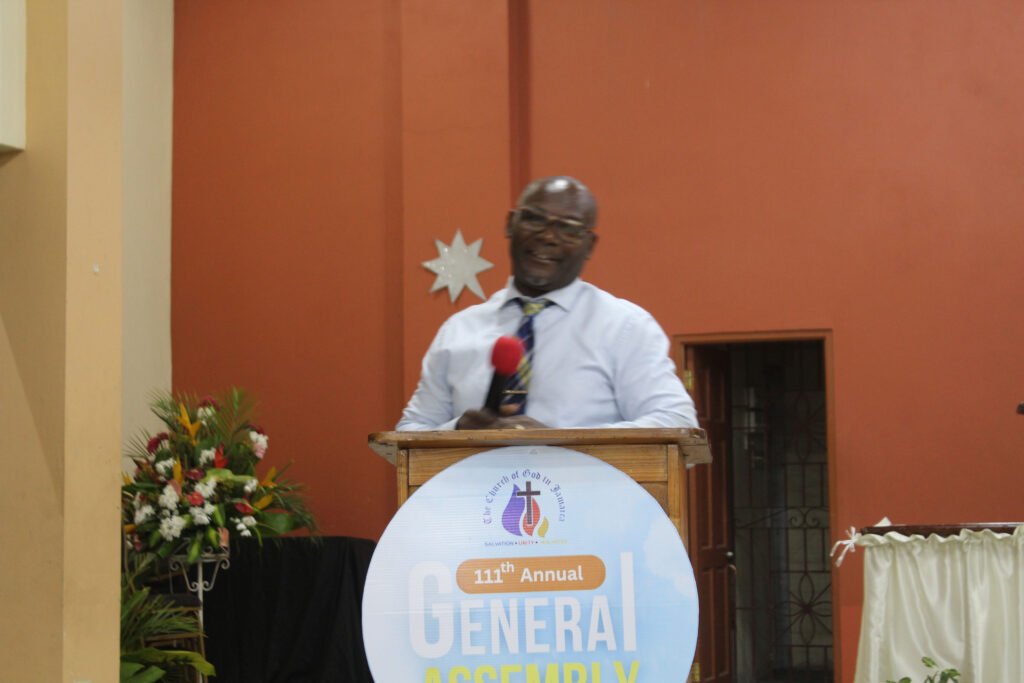 A speaker at a podium during a church event, featuring a banner for the 111th Annual General Assembly.