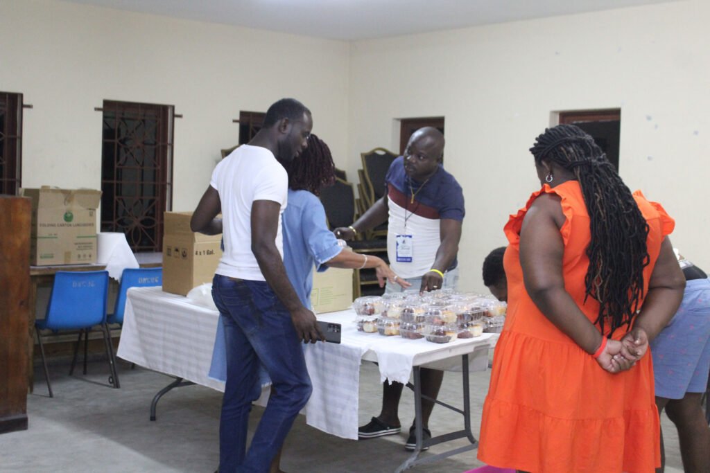 A group of people interacting around a table filled with desserts in a community setting, with various boxes nearby.